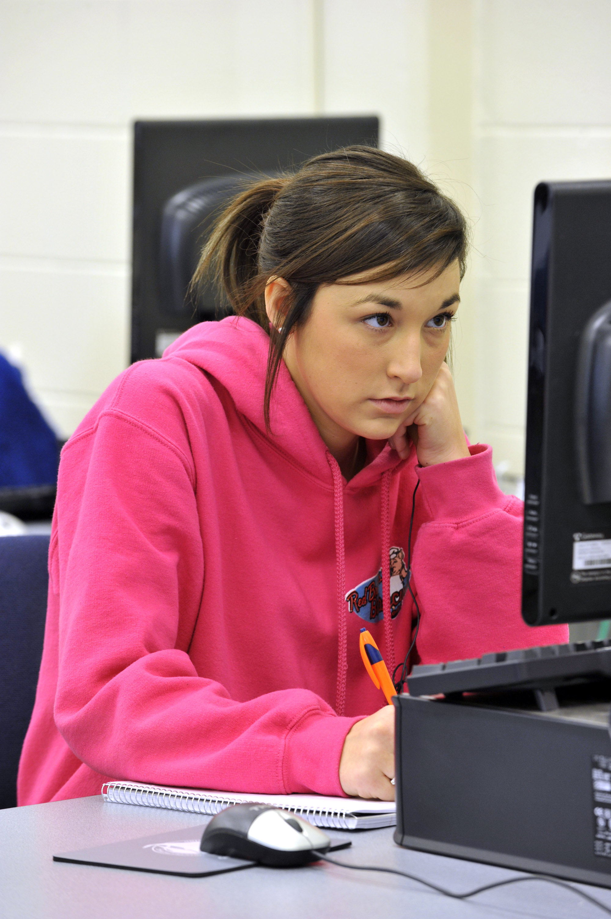 女学生在电脑室边看电脑边在笔记本上写字